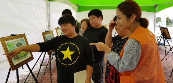 ‘2018 SK지크 레이싱 페스티벌’에 방문한 발달장애인과 가족들이 SK이노베이션 자원봉사자의 인솔 하에 전시된 그림들을 구경하고 있다. [사진=SK이노베이션]